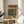 May include: Framed vintage-style Japanese poster with green and tan colors featuring turntable and cassette player illustrations, displayed on round wooden side table next to beige upholstered chair in bright sunlit room with plant shadows on white wall