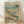 May include: Framed poster print leaning against white wall on light wood floor. Artwork shows two white ducks doing yoga poses on sandy beach - one in tree pose wearing colorful floral leggings on purple mat, another in seated position wearing striped shirt holding wine glass. Ocean waves and palm tree in background. Wine bottles, glasses, and appetizers scattered around beach scene. Vintage-style illustration in muted blues, greens, and warm tones with light wood frame.