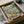 May include: Framed poster print in black frame showing three white ducks doing yoga poses on a tropical beach. One duck wears colorful floral leggings in tree pose, another in striped outfit doing warrior pose, third holds wine glass. Palm tree, ocean waves, wine bottles and appetizers scattered on sand. Vintage-style illustration with "DUCK YOGA" text at top. Print packaged in cardboard box with protective wrapping on white surface.