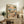 May include: Framed poster artwork displayed on rustic wooden console table beside cream armchair and potted fern. Print features cartoon cats relaxing on tropical beach - one sleeping in hammock wearing Hawaiian shirt and hat, another lounging on beach chair with sunglasses and cocktail. Beach scene includes palm trees, ocean sunset, and small sign reading "The Art of Doing Nothing." Warm peachy and blue color palette with whimsical illustration style.