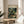 May include: Framed art print featuring Henri Rousseau's jungle scene with a leopard resting among lush green tropical foliage and white flowers, displayed on a round wooden side table next to a beige upholstered chair in a sunlit room with white walls and plant shadows.