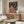 May include: Colorful poster showing two cats in astronaut suits sharing a meal at a table on an alien planet surface, with rockets and Earth visible in a starry background. Displayed above a mid-century modern walnut credenza in a bright living room with white curved chair and oval glass coffee table.