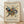 May include: Abstract geometric artwork poster in light wood frame leaning against white textured wall on wooden floor. Features colorful triangular, circular and linear shapes in blues, reds, yellows and greens on cream background. Exhibition poster format with "KANDINSKY" at top and "TATE BRITAIN EXHIBITION" text below the artwork. Soft natural lighting creates subtle shadows on wall.