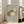 May include: Framed art print leaning against white wall next to beige armchair in bright living room. The poster features three cats in muted green and cream tones - one dark green cat with white daisy pattern, one cream cat with crosshatch texture sitting upright, and one white sleeping cat curled up. The artwork has a soft, hand-drawn illustration style on sage green background within light wood frame.