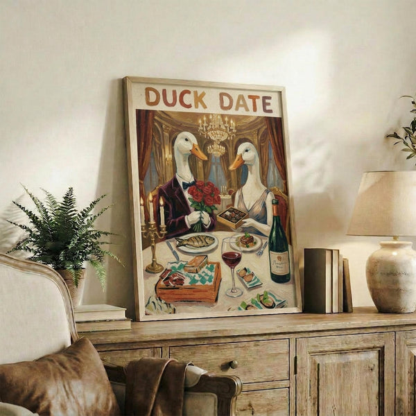 May include: Vintage-style poster showing two white ducks in formal attire dining at an elegant table with chandelier backdrop, displayed in light wood frame on rustic wooden sideboard alongside fern plant, books, ceramic vase, and brown leather furniture in cozy living room setting with cream walls.
