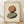 May include: Framed abstract art print featuring two balanced oval stones in earthy terracotta and sage green tones with subtle shadows, displayed in light wood frame against cream textured paper background, leaning on white wall above light wooden flooring with natural sunlight casting soft shadows across the scene.