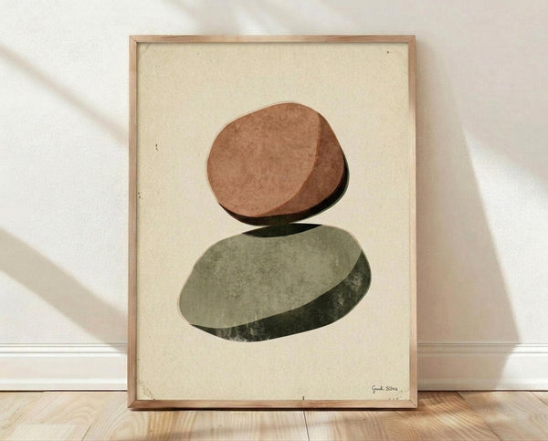 May include: Framed abstract art print featuring two balanced oval stones in earthy terracotta and sage green tones with subtle shadows, displayed in light wood frame against cream textured paper background, leaning on white wall above light wooden flooring with natural sunlight casting soft shadows across the scene.
