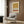May include: Modern abstract wall art print in warm terracotta, ochre yellow, and cream with dotted patterns, displayed in a contemporary living room setting with beige upholstered armchair, gold floor lamp, and wood-paneled walls