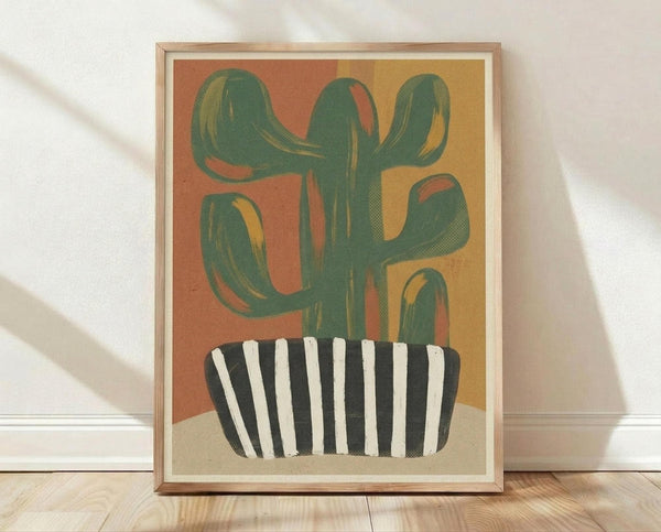 May include: Framed abstract art print leaning against white wall on light wood floor. The artwork shows a stylized green cactus with curved arms in a black and white striped pot, set against warm orange and yellow gradient background. Light wood frame with white mat. Natural lighting creates soft shadows on textured white wall.