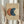 May include: Person in beige clothing holding framed abstract art print featuring three overlapping circles in terracotta orange, navy blue, and cream on textured beige background. Natural wood frame, dried pampas grass visible to left, soft neutral lighting and curtains in background.