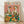 May include: Framed poster print leaning against white wall on light wood floor. Shows two anthropomorphic ducks in colorful Hawaiian shirts and hats at picnic table with wine bottles, cheese, bread basket with rubber ducklings, and roasted chicken. Pink confetti background with "DUCK PICNIC" in multicolored letters at top. Light wood frame, approximately 16x20 inches.