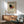 May include: Framed Kandinsky abstract art poster with geometric shapes in red, black, yellow, and blue, displayed above mid-century modern wood credenza with white ceramic lamp. Mint green upholstered armchair with wooden frame sits nearby on light wood floors. Bright natural light creates dramatic shadows on white wall, showcasing the vintage exhibition poster's bold triangles, circles, and lines in warm wooden frame.