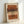 May include: Framed abstract art print leaning against white wall, featuring horizontal brushstrokes in warm terracotta, brown, beige, and peach tones with vertical column of small black dots running through center, displayed in light wood frame on neutral surface