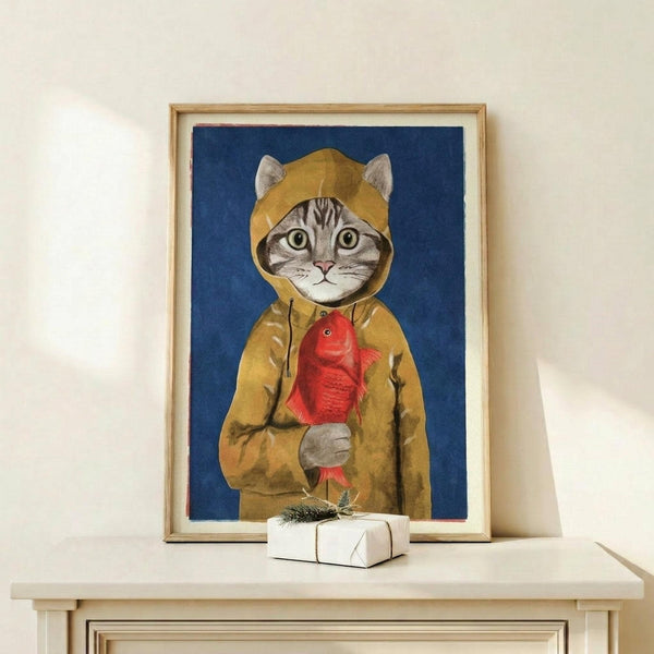 May include: Framed artwork showing a tabby cat wearing a yellow hooded raincoat and holding a red fish, set against a deep blue background. The print is displayed in a light wood frame on a white wooden surface next to a small wrapped gift with evergreen sprig. The whimsical illustration has a painted, vintage storybook style with detailed textures on the cat's fur and raincoat fabric.