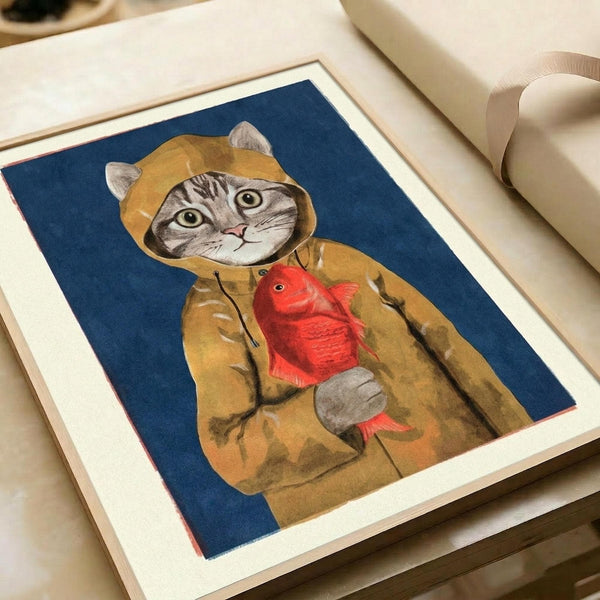 May include: Framed art print showing a tabby cat wearing a yellow hooded raincoat and holding a red fish, set against a deep blue background. The illustration has a whimsical, hand-painted style with visible brushstrokes. The print sits in a light wooden frame with white matting on a cream-colored surface next to rolled paper and ribbon.