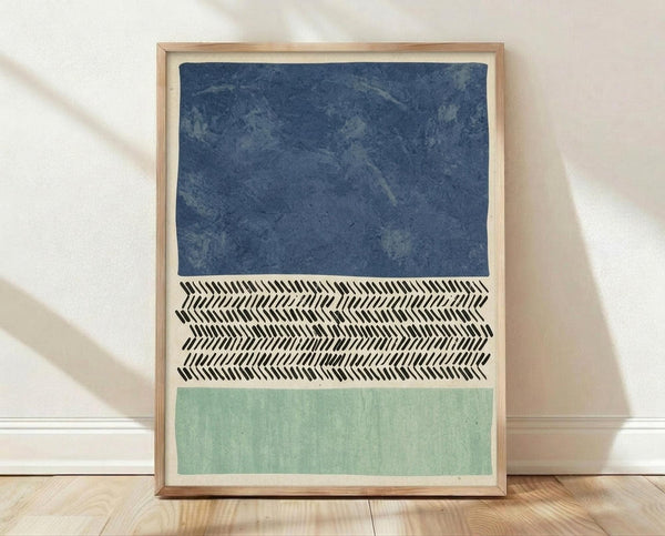 May include: Framed abstract art print leaning against white wall on light wood floor. Features three horizontal sections - textured navy blue at top, black and white herringbone chevron pattern in middle, and soft sage green at bottom. Natural wood frame with white matting. Sunlight creates diagonal shadows across the white wall.