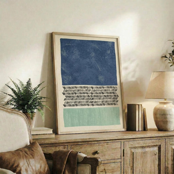 May include: Framed abstract art print with three horizontal sections - deep blue textured top, black and white herringbone pattern middle, and sage green bottom - displayed on rustic wooden sideboard alongside fern plant, ceramic vase, and books in warm neutral living room setting
