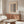May include: Beige poster with black geometric text reading "BAUHAUS" and "Ausstellung Juli - Sept 1923" displayed in thin wooden frame above mid-century walnut credenza. Modern living room setting with cream upholstered chair, glass-top oval coffee table, white table lamp, and wooden floor lamp. Neutral walls with natural lighting.