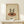 May include: Framed vintage-style poster on light wood shelf showing two silhouetted figures dancing on a red vinyl record, with "1970-1980" and "record danar love you" text below. Small white wrapped gift with evergreen sprig sits beside the natural wood frame against cream colored wall.
