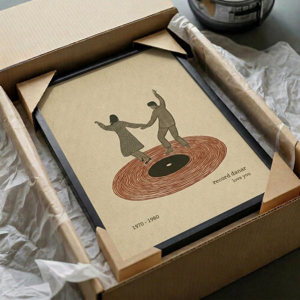 May include: Framed vintage-style poster featuring two silhouetted figures dancing on a red vinyl record, with "record dance love you" and "1970-1980" text on cream background. Black frame sits in cardboard shipping box with tissue paper, alongside wooden rolling pin and glass bowl on white surface.