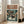 May include: Framed poster print leaning against white wall next to beige upholstered chair in bright modern living room. Artwork shows anime-style scene with small caped figure facing giant orange mech robot on rainy futuristic Tokyo street lined with glowing neon signs and tall buildings. Japanese text at top with English subtitle below. Teal and orange color palette with weathered vintage poster aesthetic in light wooden frame.
