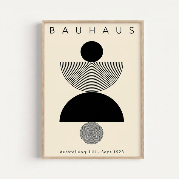 Minimalist Bauhaus-inspired poster with black geometric shapes and concentric line patterns on cream background. Features solid black circle, striped semicircle, black half-circle, and small circular pattern arranged vertically. Text reads "BAUHAUS" at top and "Ausstellung Juli - Sept 1923" at bottom. Displayed in light wooden frame against white wall.