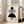 May include: Framed Bauhaus-style poster with geometric black shapes - solid circle, striped semicircle, solid semicircle, and small striped circle arranged vertically on cream background. Light wood frame leaning against white wall next to beige upholstered chair in bright, minimalist living room with large windows.