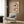 May include: Abstract floral artwork with two large brown and cream poppies on beige background, displayed in light wood frame on wood-paneled wall above cream upholstered armchair with geometric pillow. Modern reading nook with brass floor lamp and dark side table with open book.