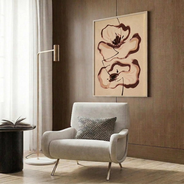 May include: Abstract floral artwork with two large brown and cream poppies on beige background, displayed in light wood frame on wood-paneled wall above cream upholstered armchair with geometric pillow. Modern reading nook with brass floor lamp and dark side table with open book.