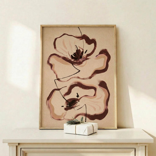 May include: framed abstract floral artwork displayed on light wood shelf against white wall. Two large stylized poppy blooms rendered in earthy brown and burgundy brushstrokes with cream petals and dark centers on beige background. Natural wood frame complements minimal styling with small white wrapped gift beside artwork.