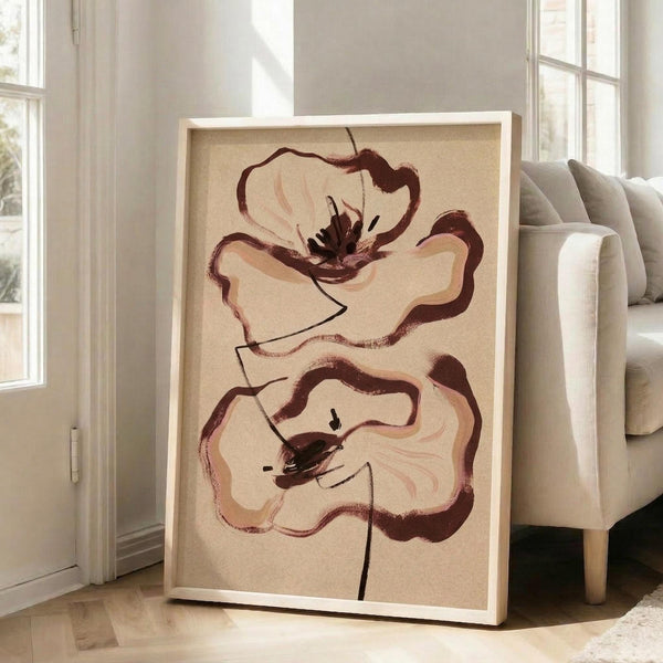 May include: Framed artwork featuring two abstract poppy flowers in earthy brown and cream tones on beige background, displayed on light hardwood floor against white wall next to beige upholstered chair with wooden legs near bright windows.