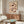 May include: Abstract floral artwork with two brown outlined poppies on cream background, displayed in thin frame above wooden sideboard. Modern living room setting with white curved chair, brass floor lamp, white mushroom table lamp, and oval glass coffee table on textured rug. Natural lighting creates warm, minimalist atmosphere.