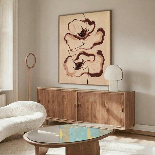 May include: Abstract floral artwork with two brown outlined poppies on cream background, displayed in thin frame above wooden sideboard. Modern living room setting with white curved chair, brass floor lamp, white mushroom table lamp, and oval glass coffee table on textured rug. Natural lighting creates warm, minimalist atmosphere.