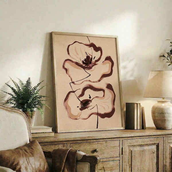 May include: Framed abstract floral artwork featuring two stylized poppies in earthy brown and burgundy tones on cream background, displayed on rustic wooden console table alongside fern plant, ceramic vase, and books in warm neutral living room setting with beige upholstered furniture