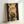 May include: Framed poster print leaning against white wall showing four overlapping golden moons in vertical alignment against starry black space background. Light wooden frame surrounds the celestial artwork with warm yellow and amber tones throughout the lunar surfaces and ethereal glow effects.