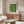 May include: Framed Bauhaus exhibition poster with green geometric circles and semicircles arranged in a grid pattern, displayed above a wooden sideboard in a minimalist living room with white curved chair, glass coffee table, and modern lamp