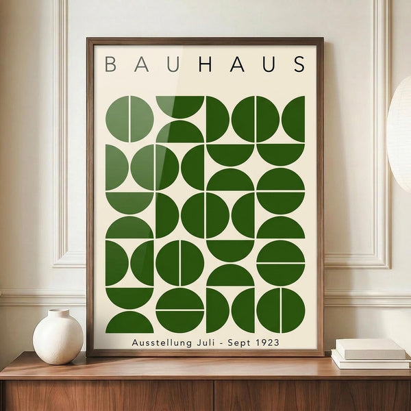 May include: Framed Bauhaus-style poster with geometric green circles and semicircles arranged in a grid pattern on cream background, displayed on wooden sideboard next to white ceramic vase and stacked books in elegant room with white paneled walls