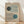May include: Framed Bauhaus-style poster with geometric design featuring two circles in dark green and teal blue intersecting with curved parallel lines on beige background, displayed in light wood frame leaning against white wall on wooden floor with natural lighting