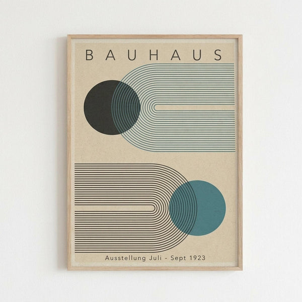 May include: Framed Bauhaus-style poster print hanging on white wall, featuring geometric design with dark green and teal blue circles intersecting curved parallel lines on cream background, text reads "BAUHAUS" at top and "Ausstellung Juli - Sept 1923" at bottom, displayed in light wood frame