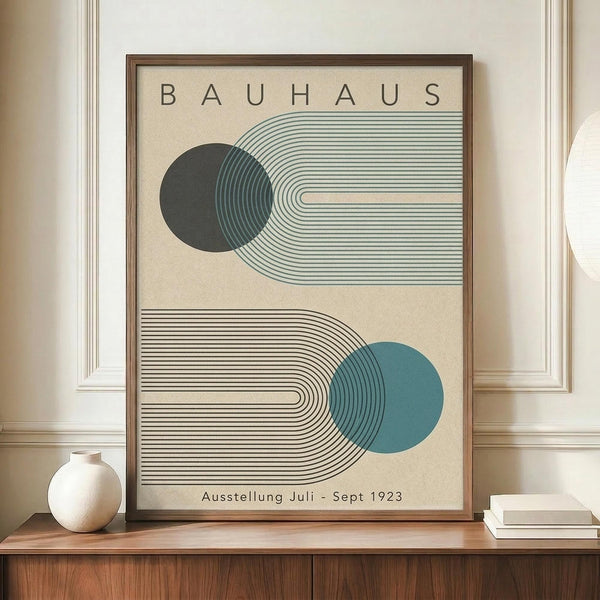 May include: Framed Bauhaus-style poster with geometric design featuring curved parallel lines forming flowing shapes around dark green and teal blue circles on cream background, displayed on wooden sideboard next to white ceramic vase and stacked books in modern interior with white paneled walls
