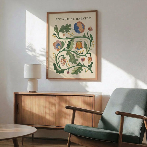 May include: Framed botanical illustration poster with "Botanical Harvest" text, featuring colorful stylized flowers and vines in blues, oranges, and greens on cream background. Shown hanging above wooden sideboard with white ceramic lamp, next to mid-century modern teal upholstered chair with wooden arms. Natural sunlight creates geometric shadows on white wall in contemporary living room setting.