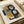 Abstract geometric artwork with layered shapes in muted tones of mustard yellow, navy blue, charcoal black, and soft gray. Bold black curved lines weave through overlapping rectangular and organic forms, creating depth and movement. The print shows visible texture and appears to be numbered, displayed flat on cream paper with gentle shadows and rolled paper visible in the background.