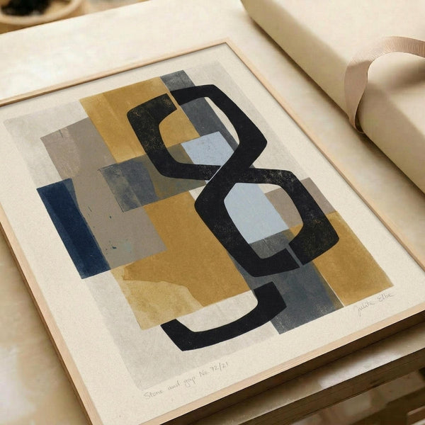 Abstract geometric artwork with layered shapes in muted tones of mustard yellow, navy blue, charcoal black, and soft gray. Bold black curved lines weave through overlapping rectangular and organic forms, creating depth and movement. The print shows visible texture and appears to be numbered, displayed flat on cream paper with gentle shadows and rolled paper visible in the background.