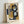 May include: Abstract geometric artwork in light wood frame leaning against white wall. Features overlapping shapes in mustard yellow, navy blue, gray, black and white with painterly textures. Bold black curved forms create flowing movement through layered rectangular color blocks. Signed print with visible artist signature at bottom.
