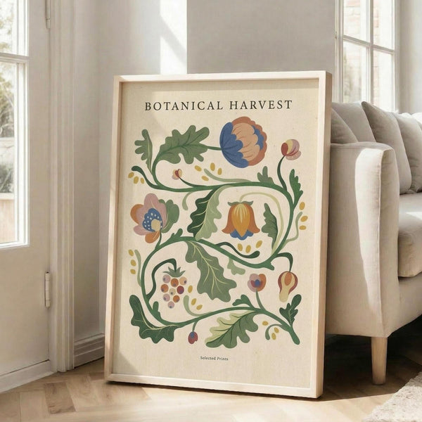 May include: Large framed botanical illustration poster leaning against white wall next to beige sofa. The artwork features decorative flowering vines with blue, orange, and pink blooms, green foliage, grapes, and ornamental elements on cream background. Natural wood frame, bright room with large windows, hardwood floors.