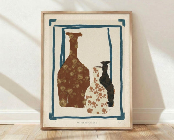 May include: Framed art print leaning against white wall on light wood floor. Print shows three pottery vessels - brown bottle with small dots, white vase with rust spots, and dark narrow vessel - surrounded by teal blue painted border on cream background. Natural wood frame with white matting. Soft natural lighting creates diagonal shadows on wall.