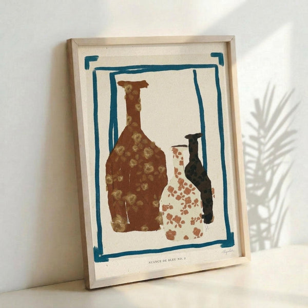 May include: Framed abstract art print featuring three pottery vessels in earth tones - a large brown bottle with golden dots, a white vase with terracotta speckles, and a dark narrow bottle. Blue painted border frames the still life composition on cream paper. Natural wood frame leans against white wall next to dried palm frond shadow.