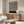 May include: Black and white swirling geometric pattern poster with Bauhaus text mounted above a mid-century modern wooden credenza. Room features white textured chair, glass-top coffee table, and warm natural lighting creating shadows on light walls.