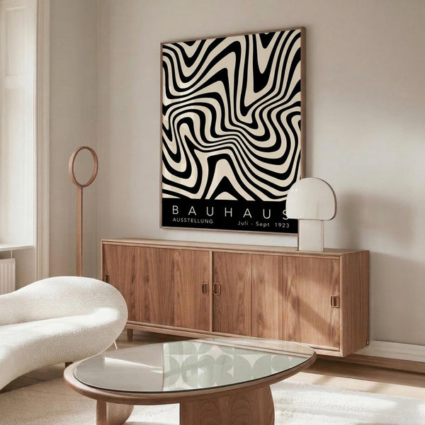 May include: Black and white swirling geometric pattern poster with Bauhaus text mounted above a mid-century modern wooden credenza. Room features white textured chair, glass-top coffee table, and warm natural lighting creating shadows on light walls.