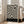 May include: Black and white abstract swirling pattern poster with curved flowing lines creating an optical illusion effect, displayed in light wood frame leaning against white wall next to beige upholstered sofa in bright living room with large windows and natural lighting on hardwood floors.